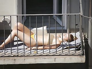 Student in bikini sunbathing on the balcony